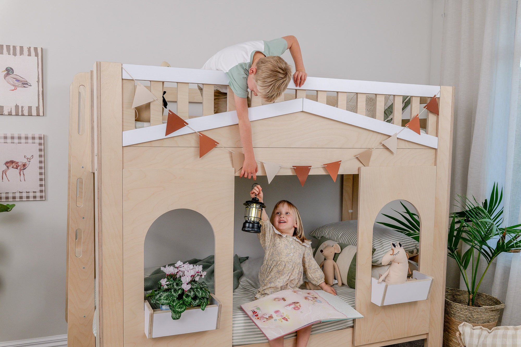 Children playing on a wooden playhouse bed in a room with plants and decor.